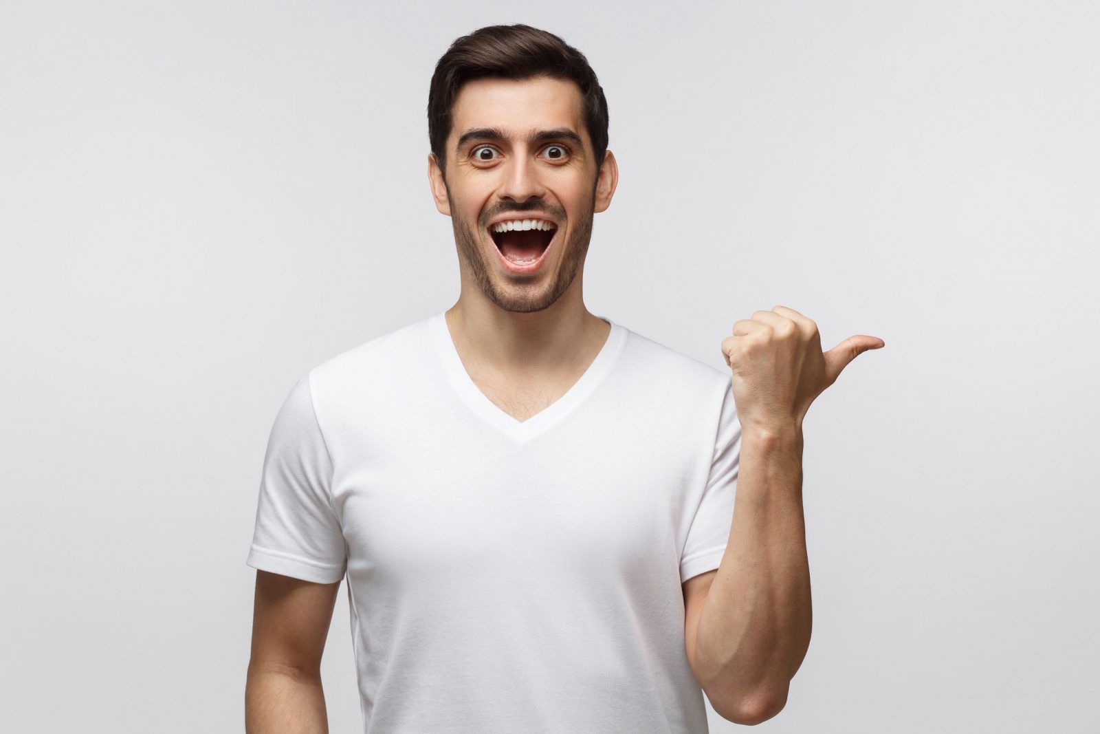 Young surprised man in white t-shirt pointing right with his finger