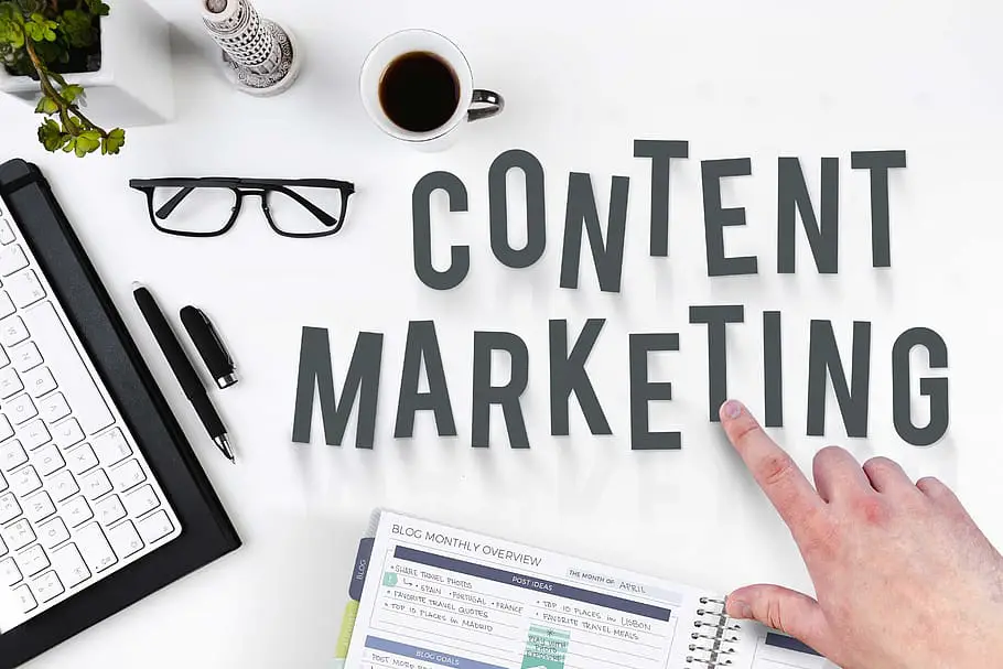 A finger pointing at text saying ‘content marketing’ surrounded by a laptop and coffee.