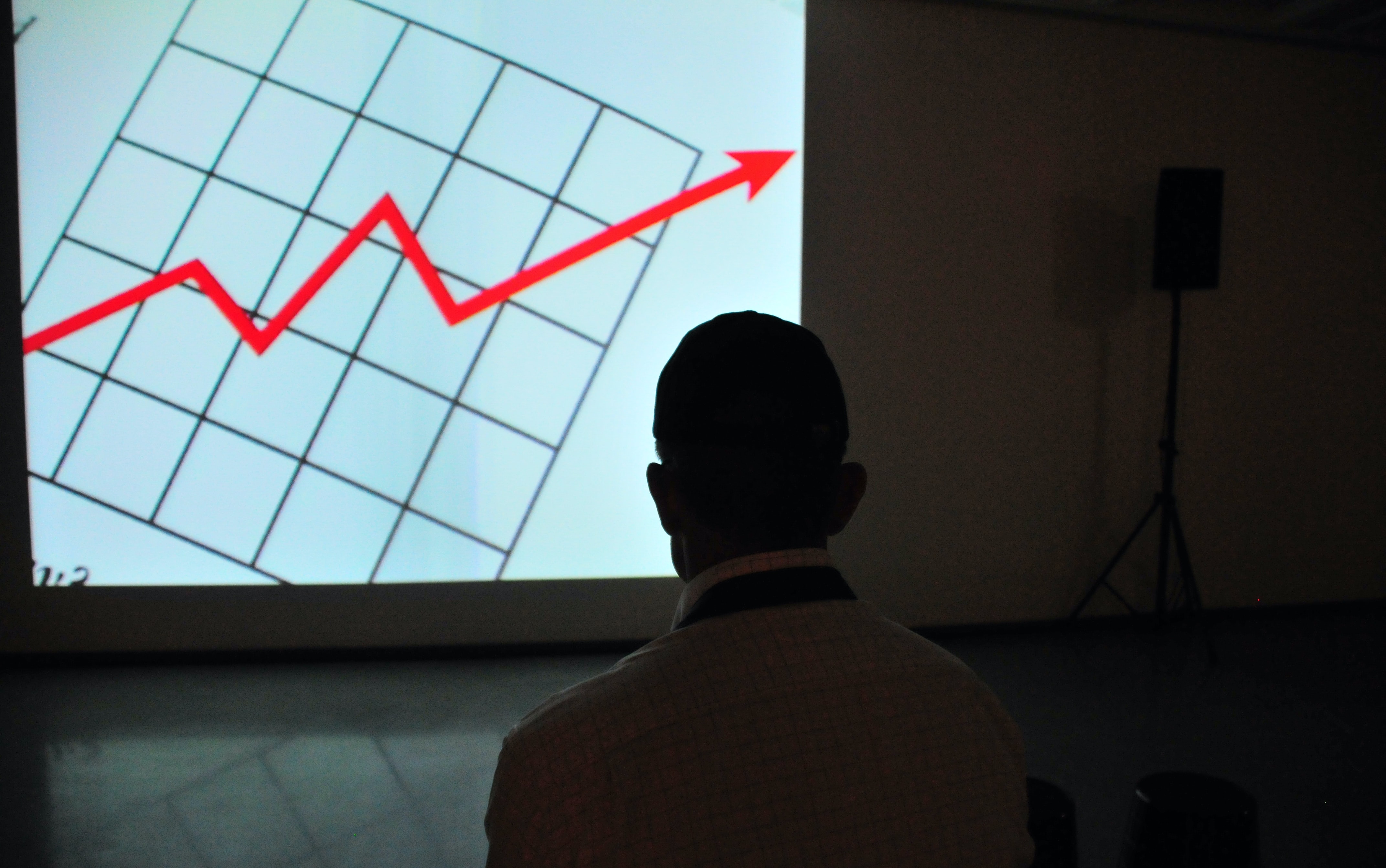 A businessman looks at a projector showing positive growth.