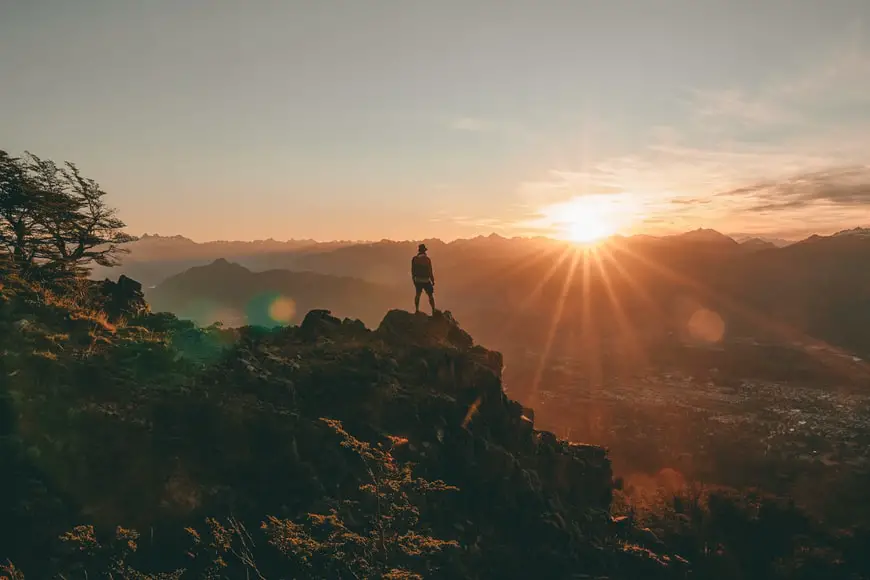 A hiker stands overlooking a cliff during a beautiful sunset.